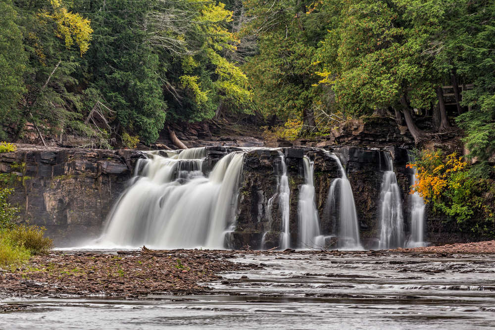 Water cascading down a rock cliff with foliage in the background on the beautiful Manabezho River, one of the waterfalls in Michigan