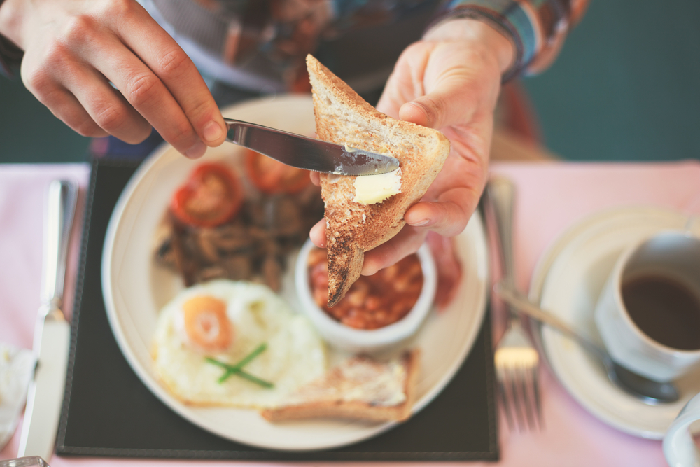 A person buttering toast with a cooked breakfast out of focus