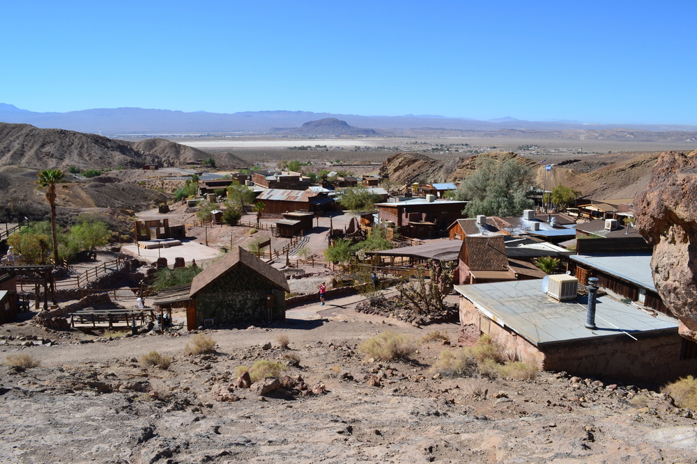 A view of the Calico Ghost Town in the desert of California. There are several old buildings scattered around the desert and walkways to get to them. In the distance you can see some mountains. Route 66 attractions