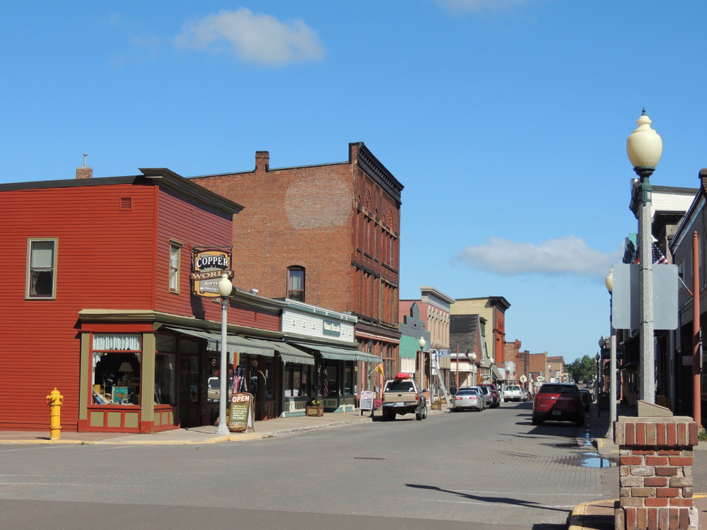 A street view of the historic town of Calumet. There are historic buildings and shops with cars parked on the side of the street.