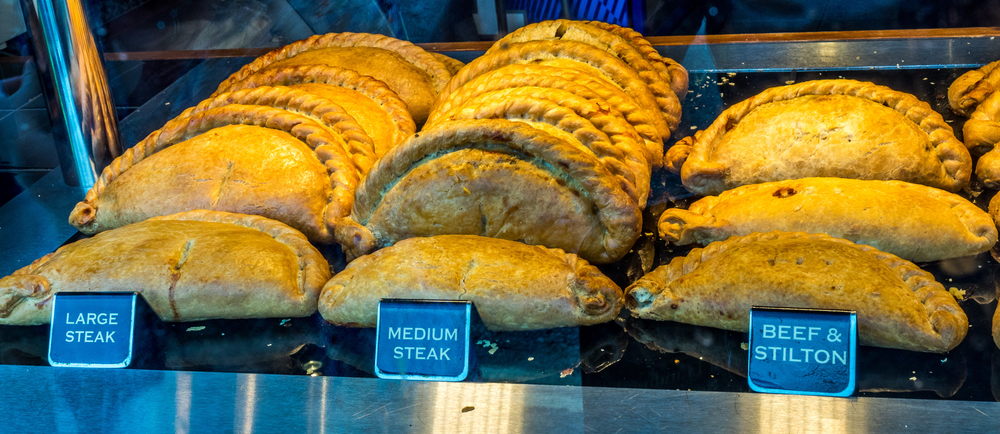 A tray of Cornish Pasties which are a pastry that are folded in half with braided edges and stuffed with meat and vegetables. The pasties are separated by 'large steak' 'medium steak' and 'beef and stilton' flavors. 