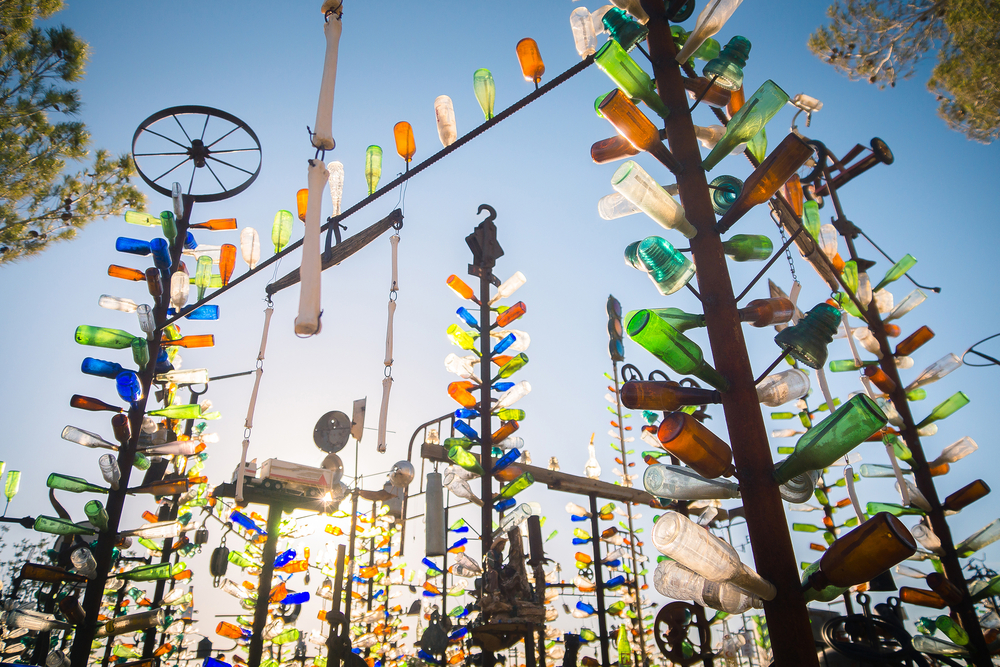 Large metal poles with bottles of all different colors attached to them. The sun shines through them and it is a clear blue sky. 