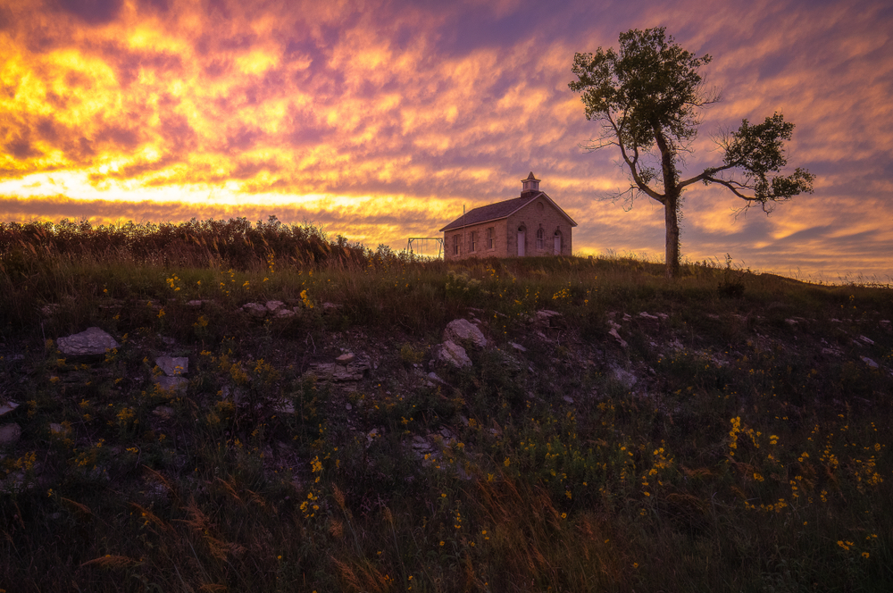 Sunset over the brick schoolhouse at Tallgrass Preserve with yellow flowers in the foreground.