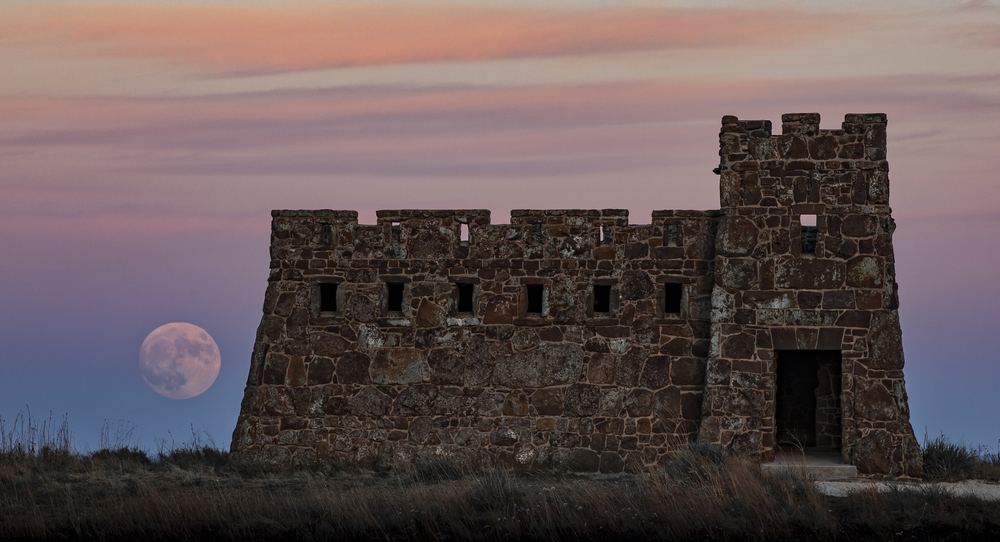 A castle with a hige moon and sunset in the background.