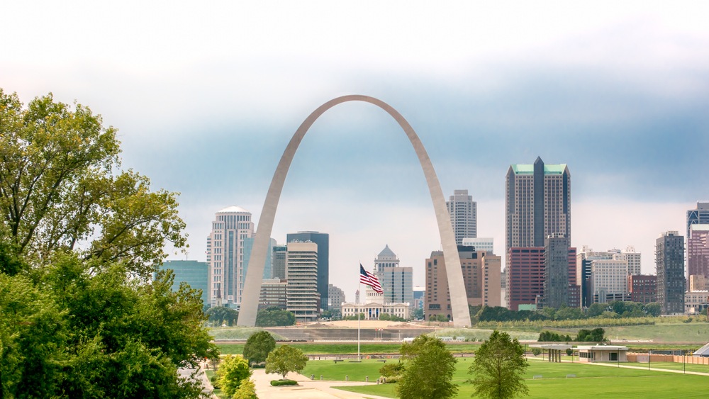 Large arch with city skyscrapers in background and American flag in foreground. 