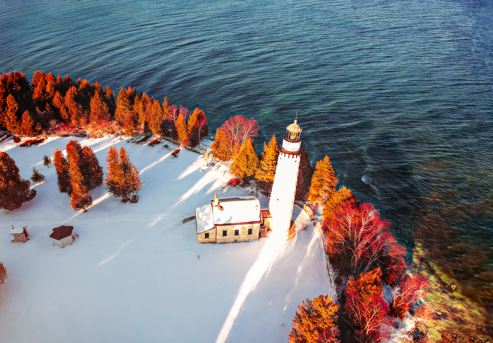 A island with fall foliage and a lighthouse all covered in snow.