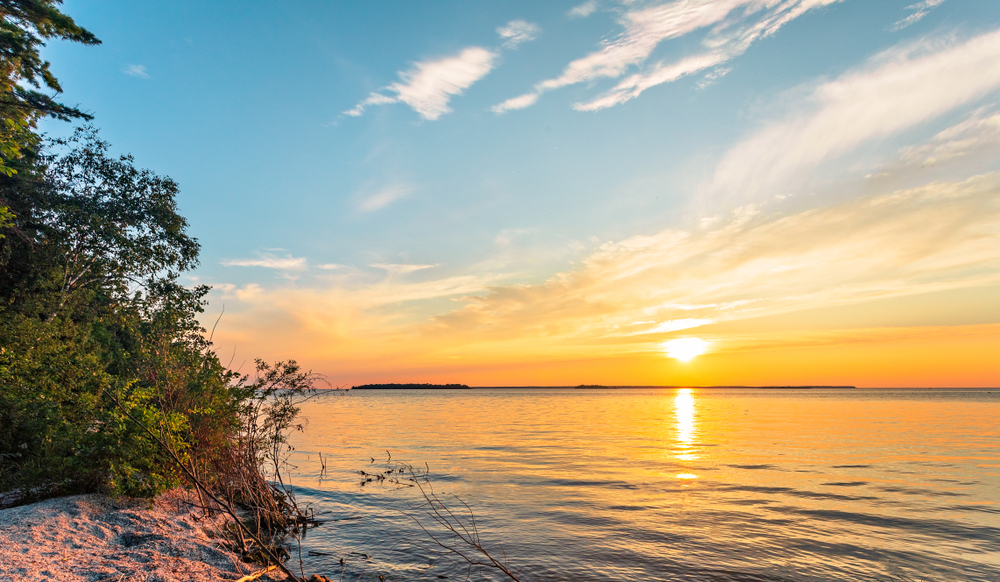 Sunset from a beach with trees in the foreground in an article about things to do in Door County