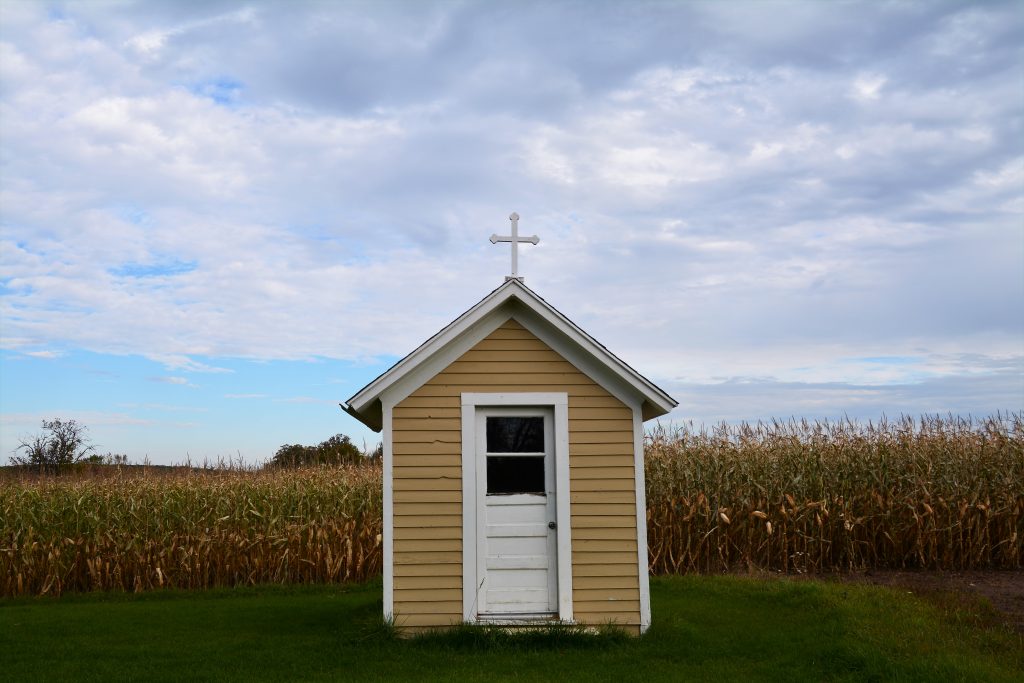 A small yellow and white wayside chapel with a corn field in the background things to do in Door County Wisconsin
