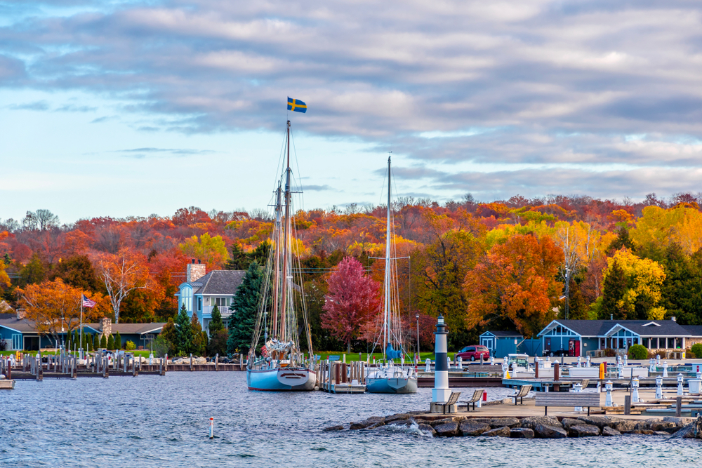 A waterfront town with a hrabout and beautiful fall foliage in the background.