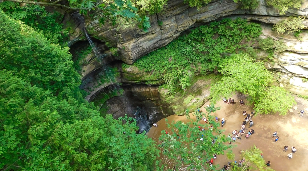 Water pouring off a ledge into a rounded canyon below with people stood at the foot watching.
