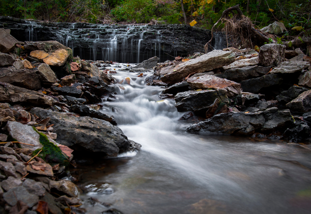 waterfalls cascading down 10 foot drop and flowing into stream below.