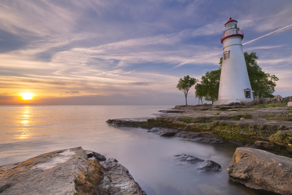 A lighthouse is pictured on a peninsula as the sun sets on Lake Eerie in one of the prettiest state parks in Ohio.  