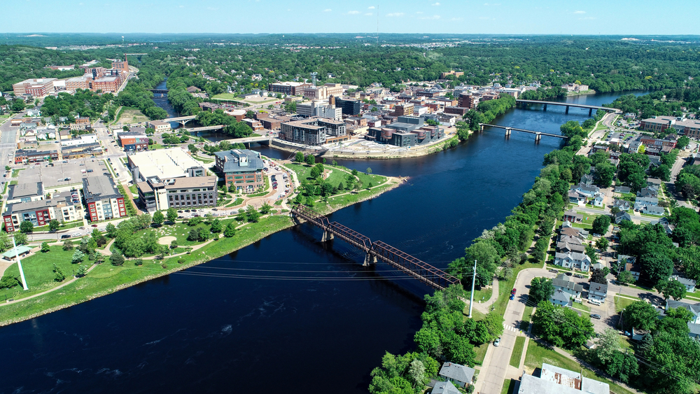 An aerial view of the college town Eau Claire, a town on the edge of the Mississippi River. There are lots of tall buildings and homes surrounded by trees.