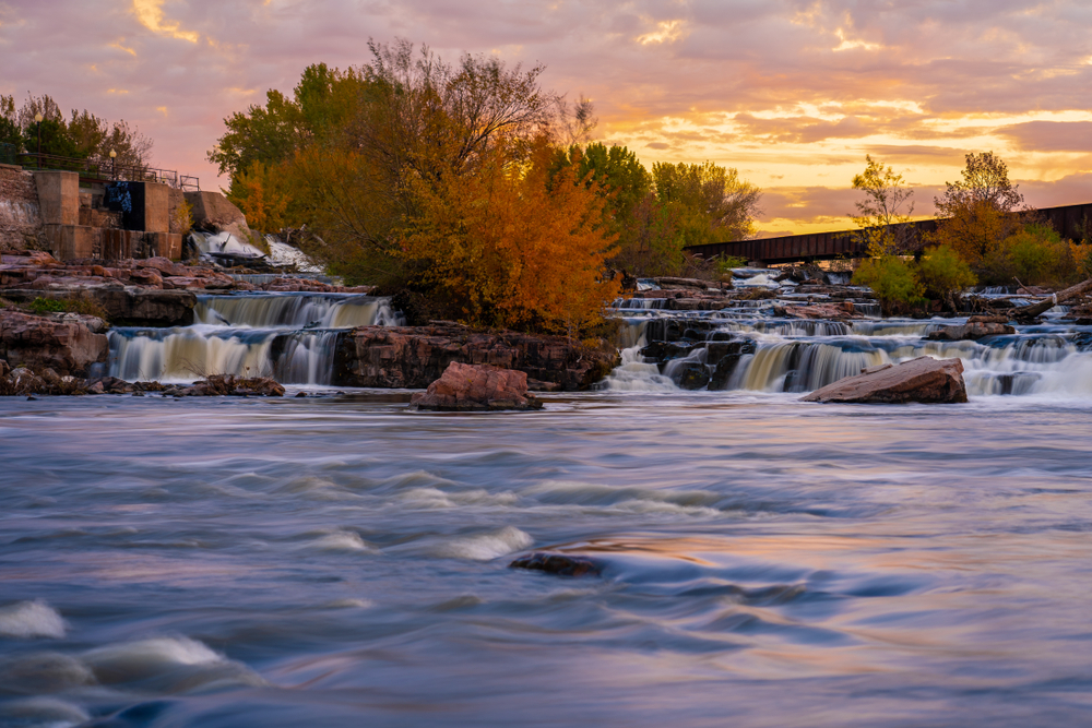 fall  in south dakota on display with waterfalls, orange leaves on trees in autumn and orange sunset in background.