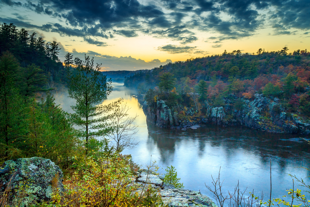 A misty river surrounded be small cliffs and fall foliage