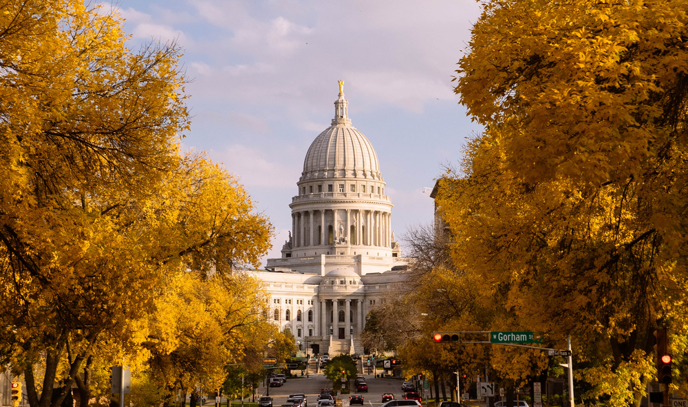 Looking down a tree lined road towards the capital building in Madison Wisconsin. The trees have yellow leaves and the building is a large white colonial style building. Awesome for Wisconsin weekend getaways