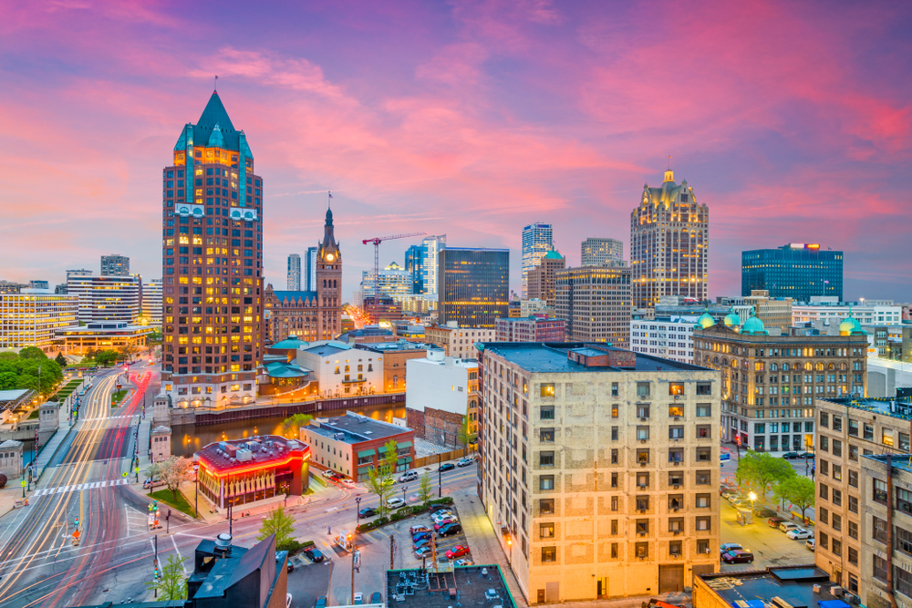 The city skyline of Milwaukee at twilight, one of the best Wisconsin weekend getaways. The buildings are all lit up and the sky is pink, purple, and blue.