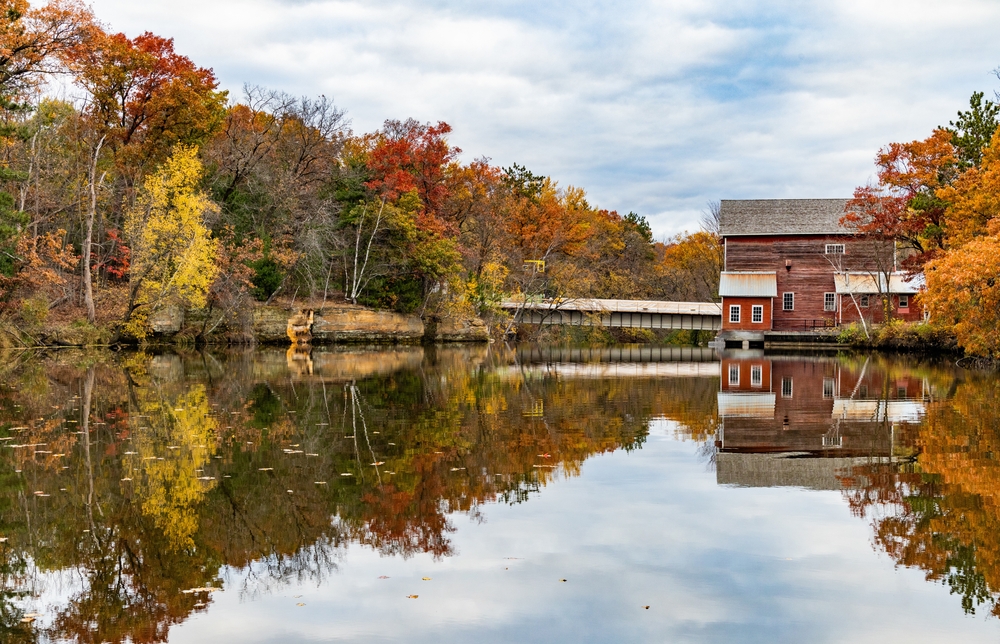 Scenic fall colors at Dells Mill Pond you can see the mill the water a bridge and the fall trees. The article is about the best Wisconsin weekend getaway.