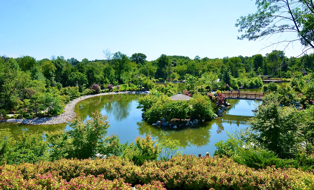 A view of one of the gardens at the Frederik Meijer Gardens & Sculpture Park. There is a small pond with a bridge across it, a gazebo, and of course lots of greenery. The bridge and trees are reflected in the pond. One of the best things to do in Michigan.