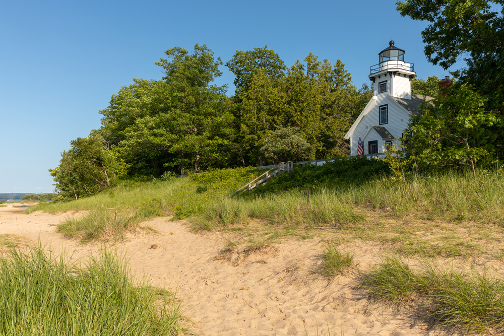 A beqach and grass with a lighthouse in the background