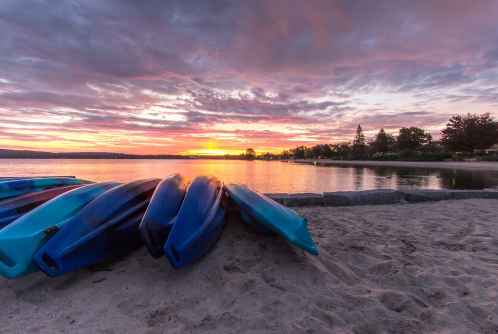 Kayaks on the sand with the water and tress in the background. Clinch Park has one of the best beaches in Traverse City