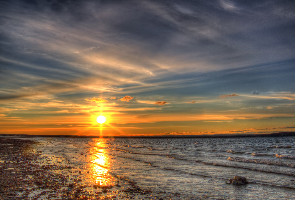 East bay at sunset with the sun reflecting on the water and the beach. One of the beaches in Traverse City