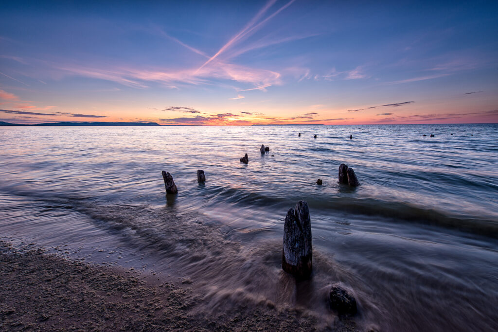 Sunset in background with orange sky and blue water in foreground.