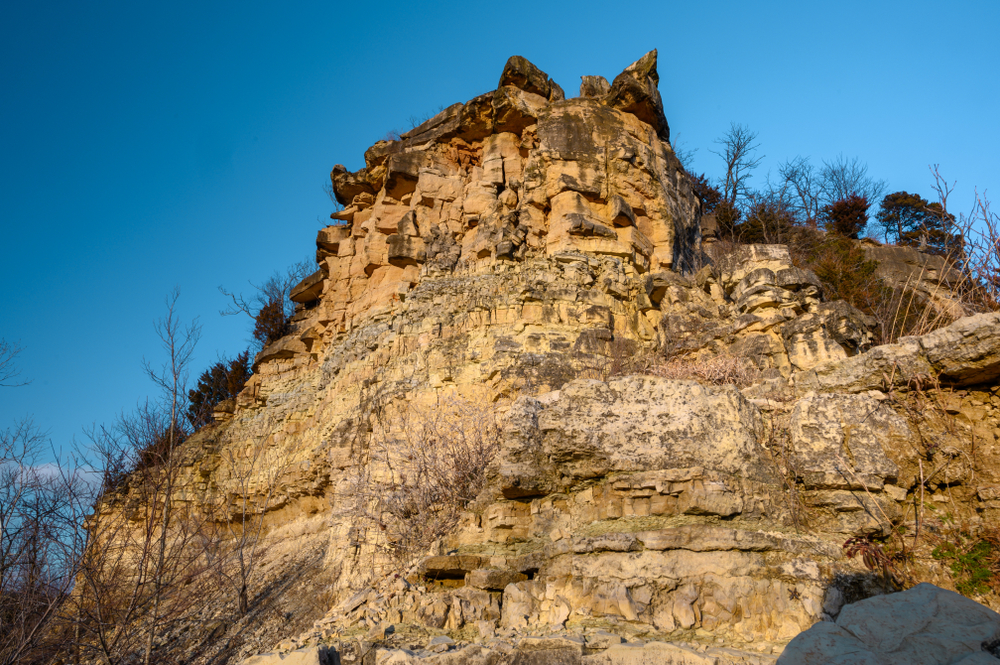 The larges stone bluff at Klondike Park. It is a sandy color stone and has trees with no leaves or brown leaves all over it. The sky is very blue. 