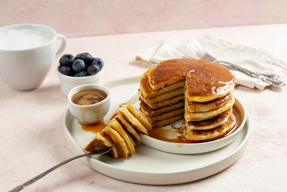 Pancakes piled high on a plate with blueberries and maple syrup