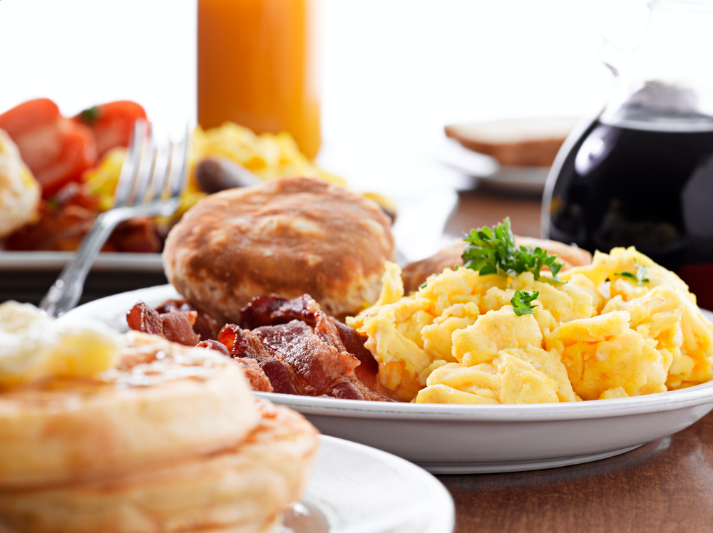 A huge american breakfast with eggs and biscuits on a table with coffee and crumpets