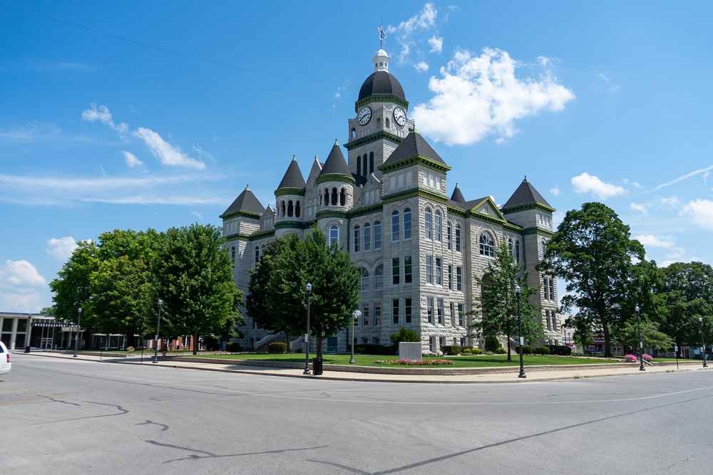 The court house in the small town of Carthage. It is a large stone building with gray stone, green trim, and a clock tower. Around it is a green lawn and trees. One of the best Missouri road trips stops