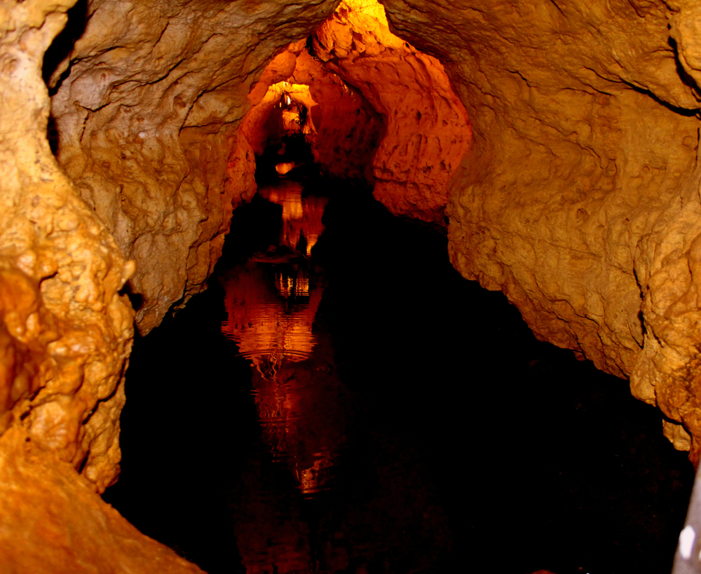 Looking down one of the cave tunnels in the Cave of the Mounds, one of the best things to do in Wisconsin. The rocks are yellow and orange. There are lights on some of the rocks and there is water in the tunnel. 