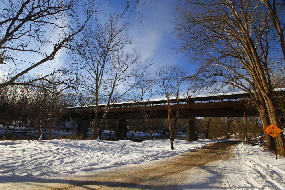 A brown covered bridge in the winter with snow on the ground