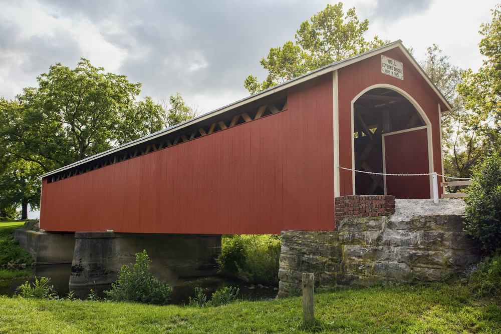 A red bridge with white trim on a brick plinth over a river