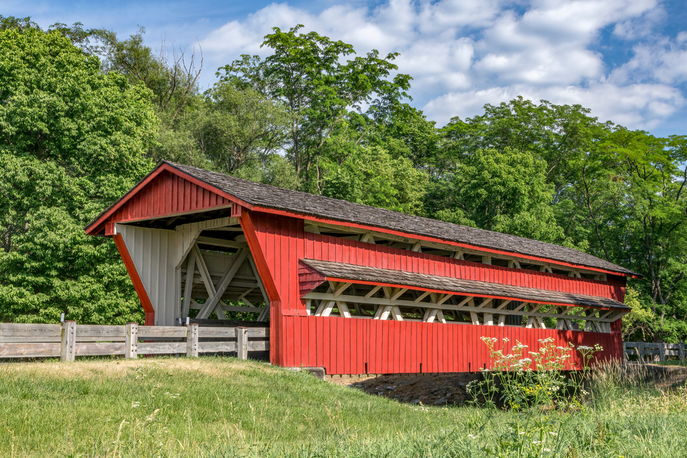 A red covered bridge over a creek with grass and trees around.