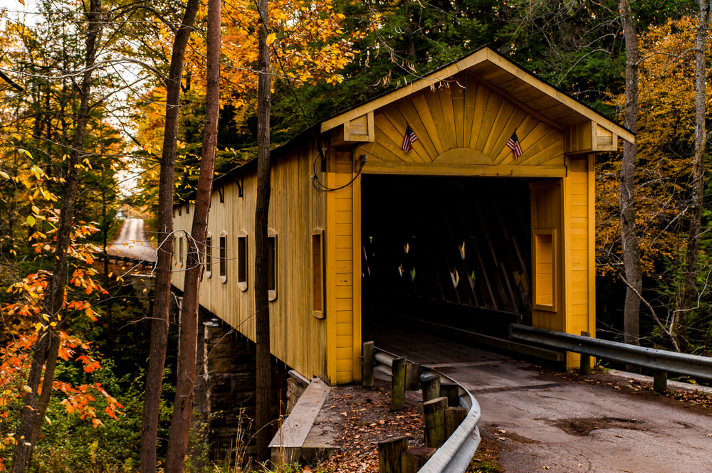 A yellow colored bridge on a road in the autumn foliage. Windsor Mills in one of the covered bridges in Ohio