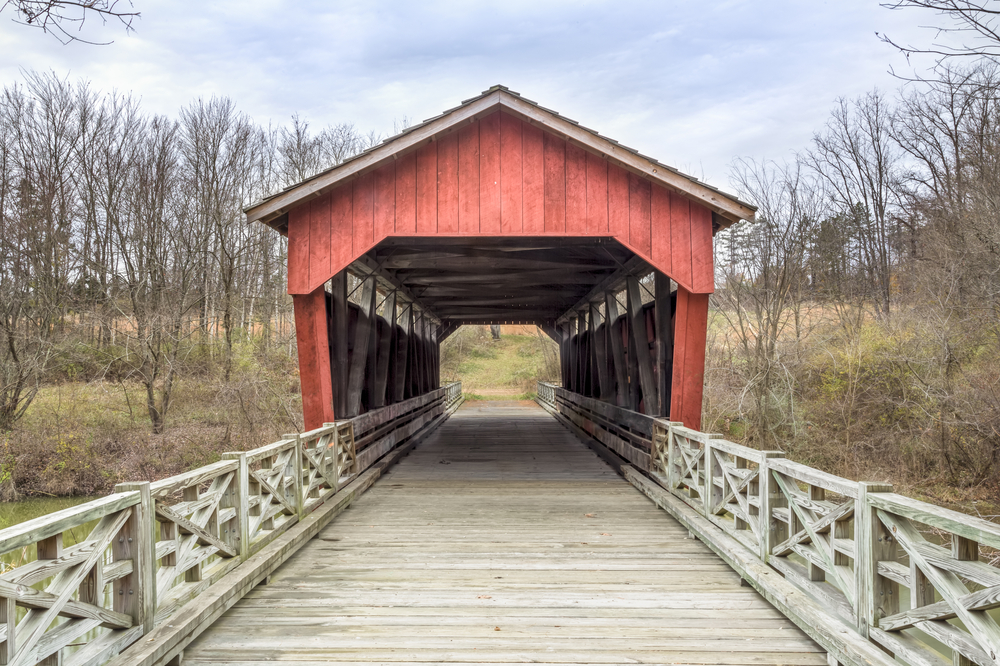 A red covered bridge in ohio with trees in the background.