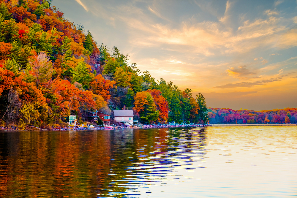 The view from the water of the shore of the Devil Lake State Park. On the shore is a building with boats around it. There are also tons of trees with red, orange, yellow, and green leaves. One of the best things to do in Wisconsin.