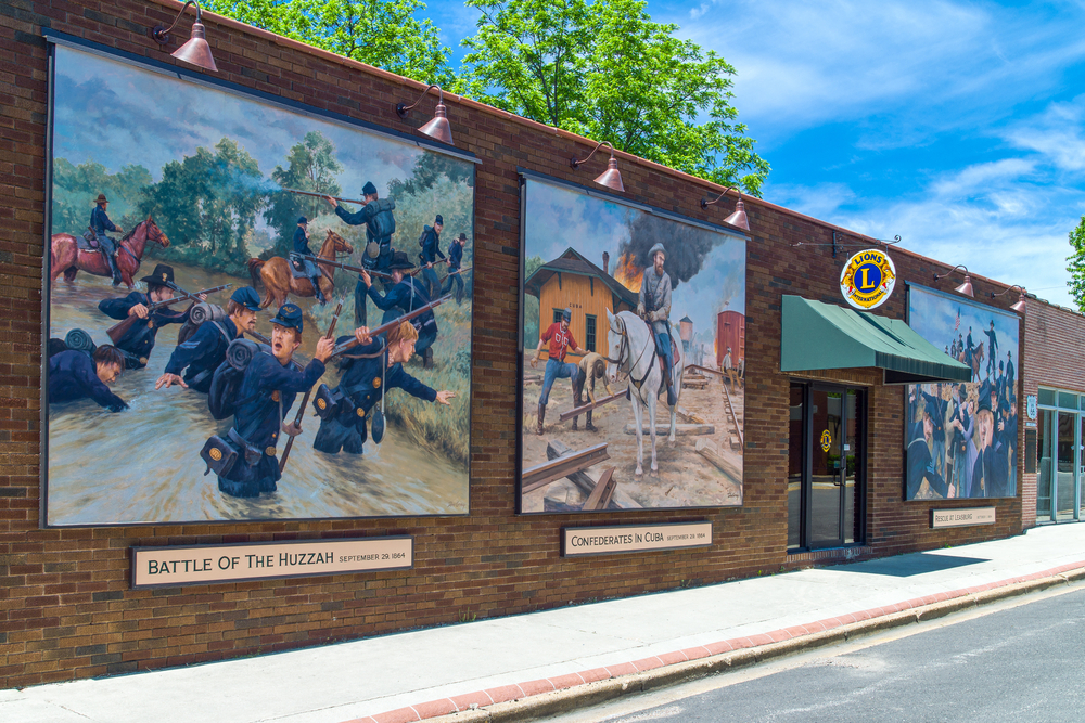 A brick building with three painted murals on the side of it. The murals depict different scenes like a battle scene and a man riding a horse. A great stop on any Missouri road trips 