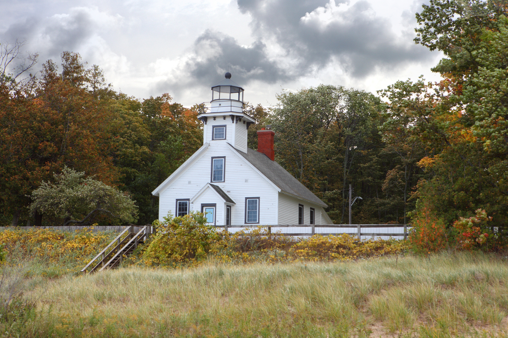 an old white lighthouse. Old Mission Point Lighthouse surrounded by grass and foliage