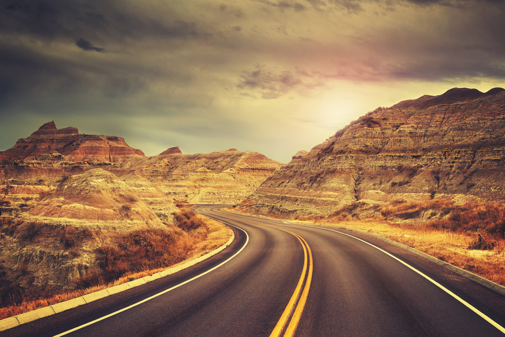 Scenic two lane asphalt highway surrounded by tall orange rocky bluffs on either side.