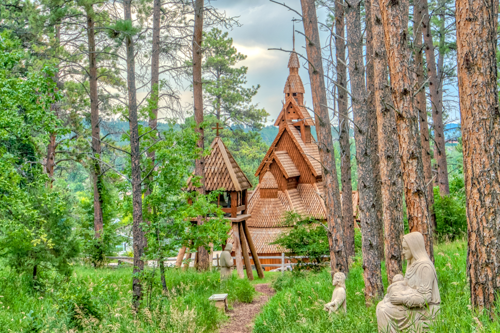 The Chapel in the Hills in Rapid City, South Dakota: wooden church nestled in forest. Religious statues in foreground.