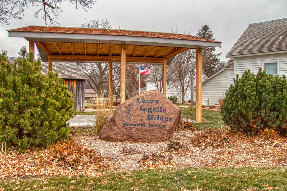 Large boulder inscribed with wording:  Laura Ingalls Wilder Memorial Society under wooden pergola on property. South Dakota attraction not to miss.