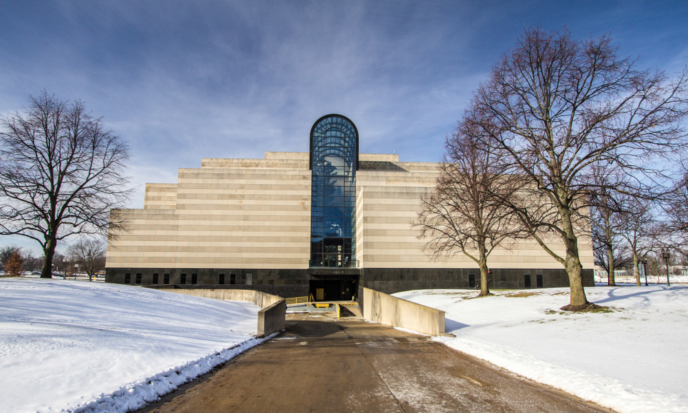 A concrete building with a glass atrium and snow around it. Visiting the History Museum is one of the things to do in Lansing MI