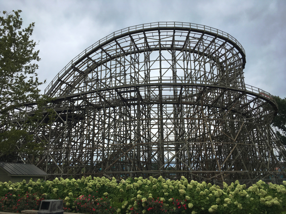 Looking at a wooden rollercoaster. The sky is dark and there are a few trees near the rollercoaster. 