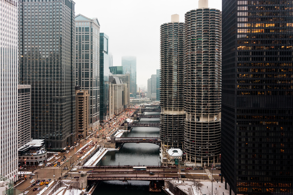 Looking down the Chicago River on a snowy winter day. There is snow on the ground and the river looks frozen. It is an overcast grey day. 