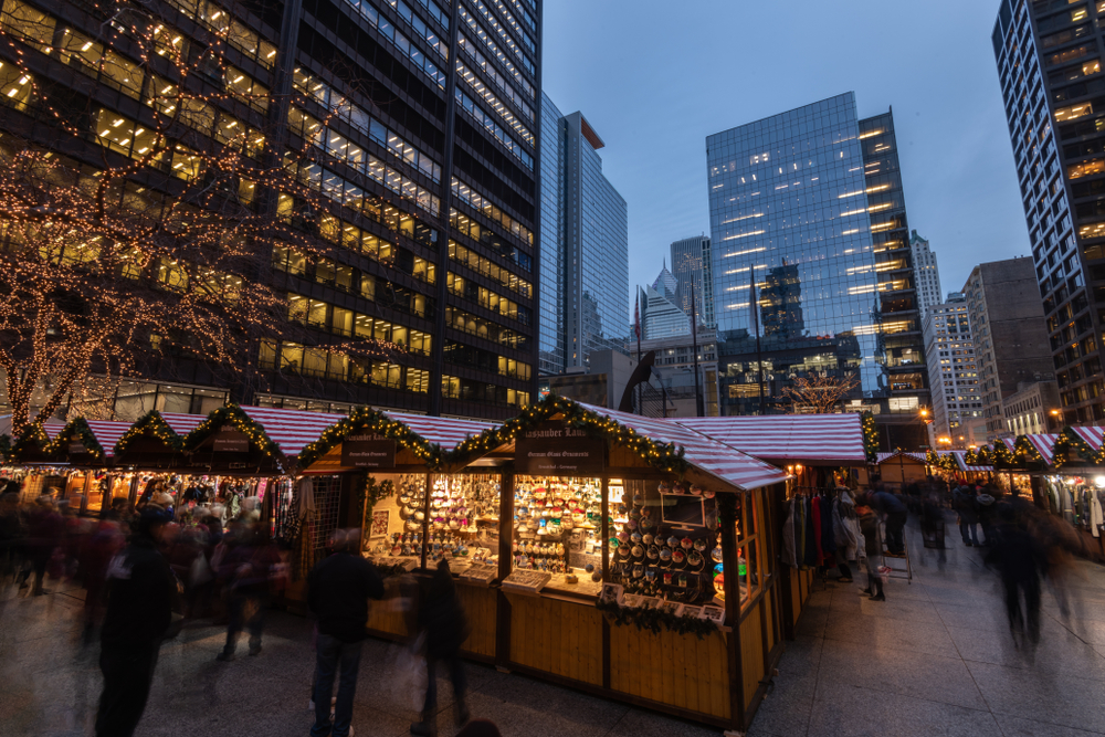 A Christmas market in downtown Chicago at Christmas time. It is twilight and the little shops are all lit up from inside. There are twinkle lights on them and on the trees in the park. One of the best things to do at Christmas in Chicago. 