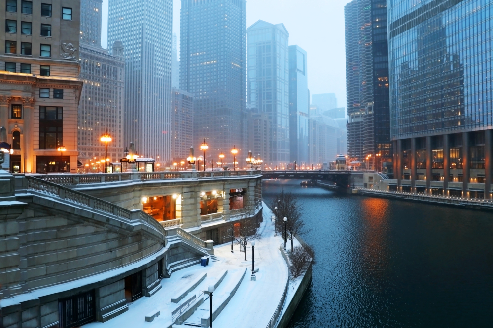 A foggy day winter day in Chicago. There is snow on the ground, the street lights are on, and you can see the Chicago River which looks frozen. 