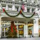 A large ornate shopping district entrance of the Magnificent Mile in Chicago. In the middle of the ornate arch way entrance is a large Christmas tree lit up with a big red bow on it. There is also a sway of greenery with red bows and lights hanging on the archway.