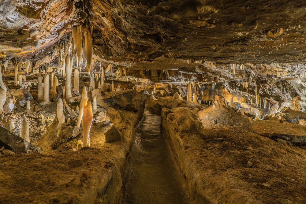 Looking down a narrow path inside a cavern in Ohio. You can see interest rock formations from both the top and bottom of the cavern that creates an optical illusion. The rocks are different shades of tan.